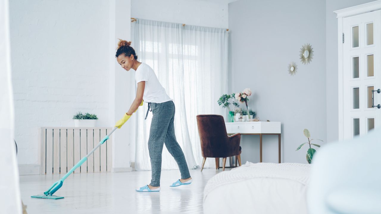 A woman cleaning a bright, modern living room with a mop, creating a clean, welcoming space.