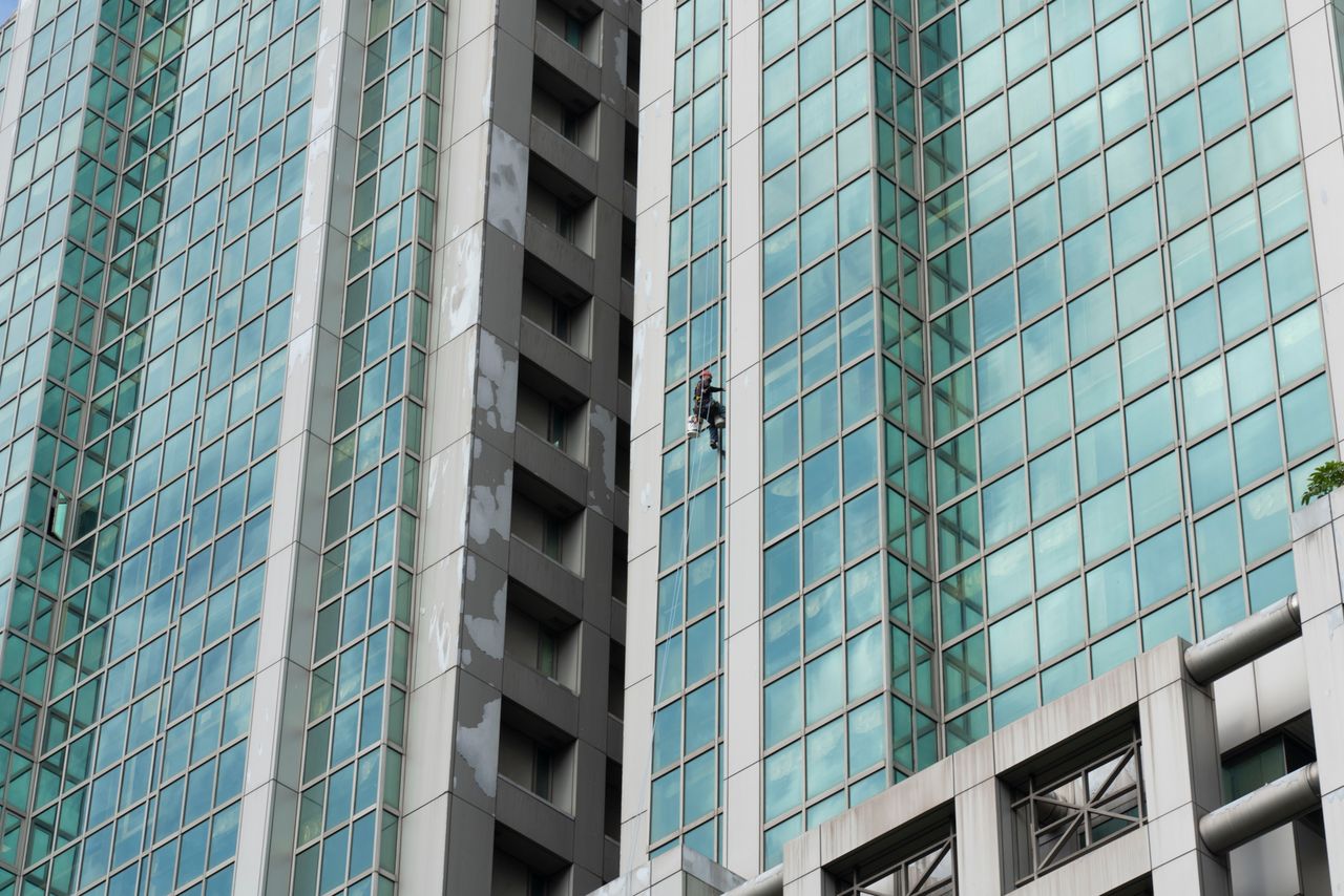 A worker cleans the glass windows of a tall skyscraper using harness and ropes.